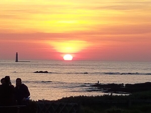 Un atardecer sobre el océano con un faro a lo lejos.