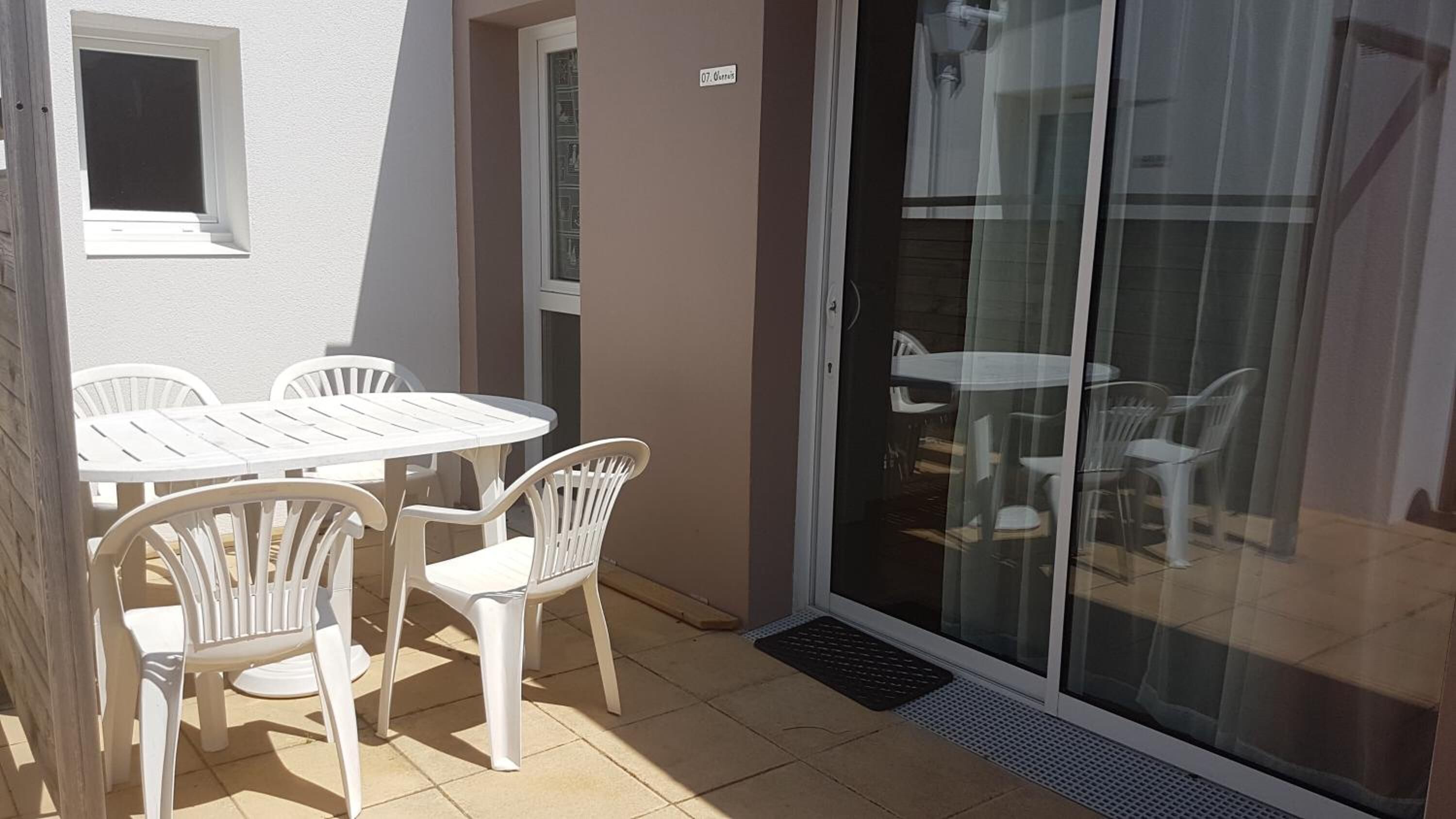 Un'area patio con tavolo e sedie bianche, una porta scorrevole in vetro e una piccola finestra.
