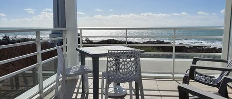 A balcony with a table and chairs, overlooking the ocean with a clear sky.