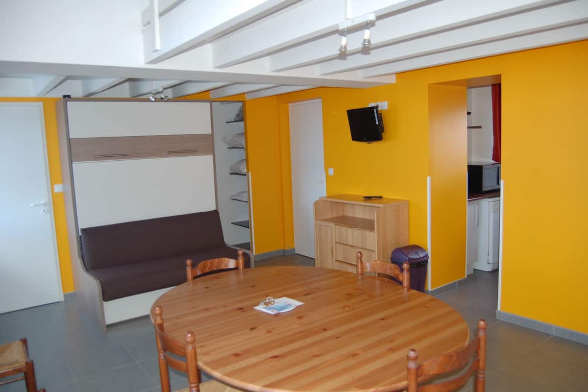 Une pièce avec une table ronde en bois, un canapé marron et un téléviseur fixé au mur.
