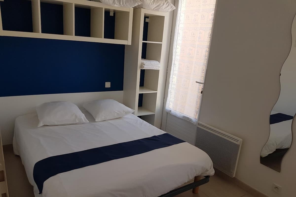 Une chambre à coucher comprenant un lit, des étagères intégrées, une fenêtre avec un rideau et un radiateur.