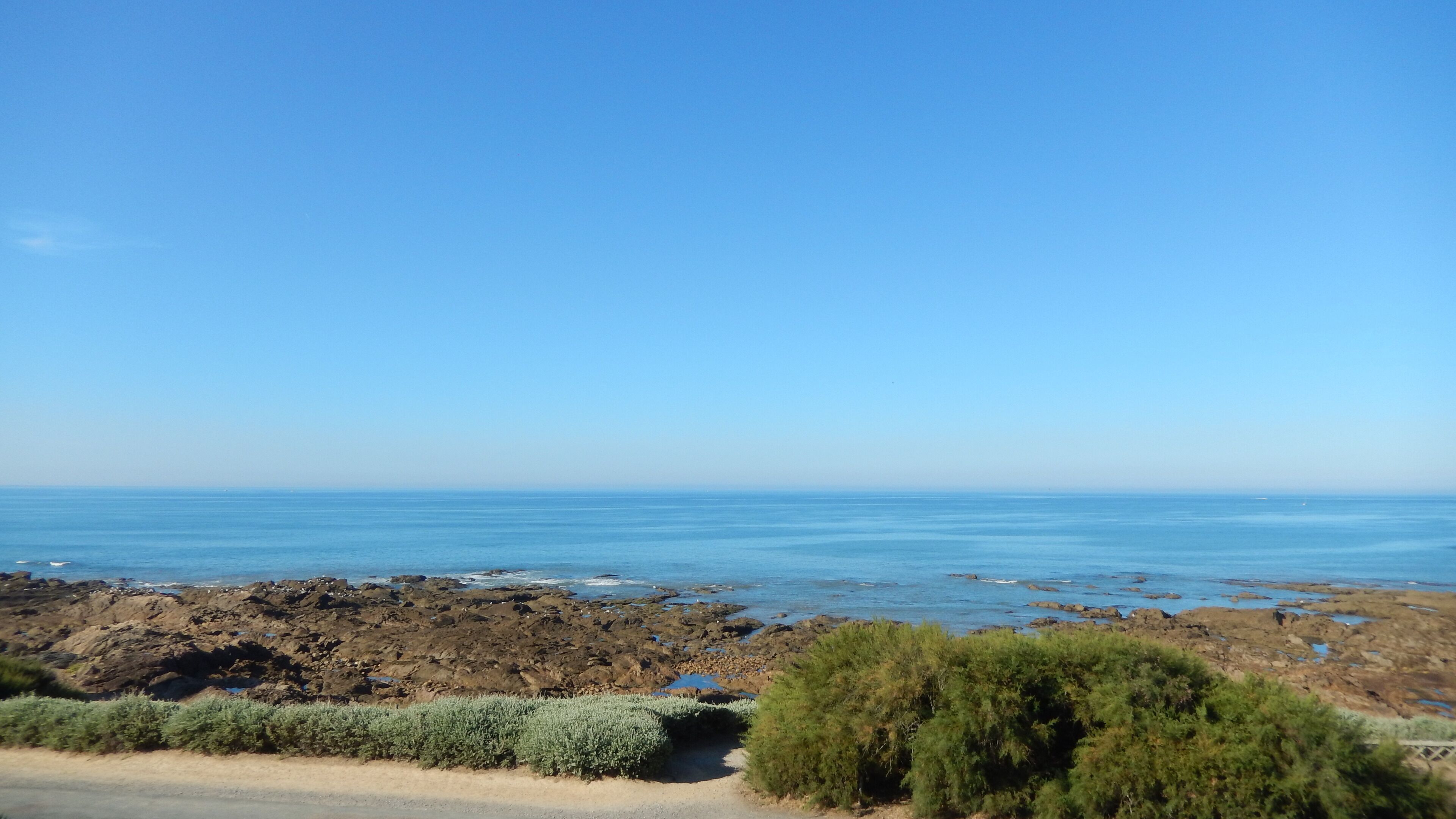 A coastal landscape with rocky terrain and a clear blue sky.