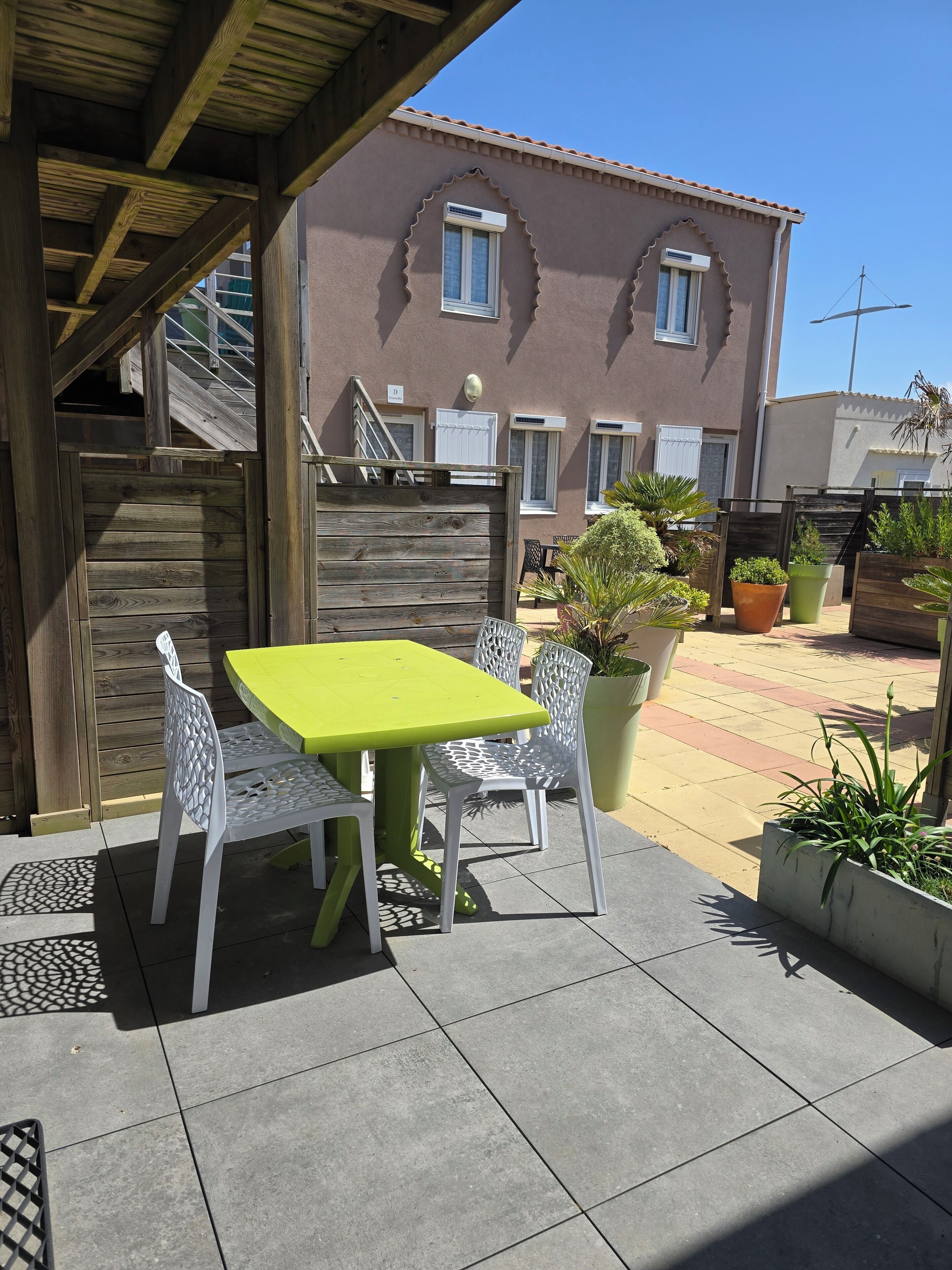 Un patio con una mesa y sillas, una cerca de madera y un edificio con ventanas arqueadas al fondo.