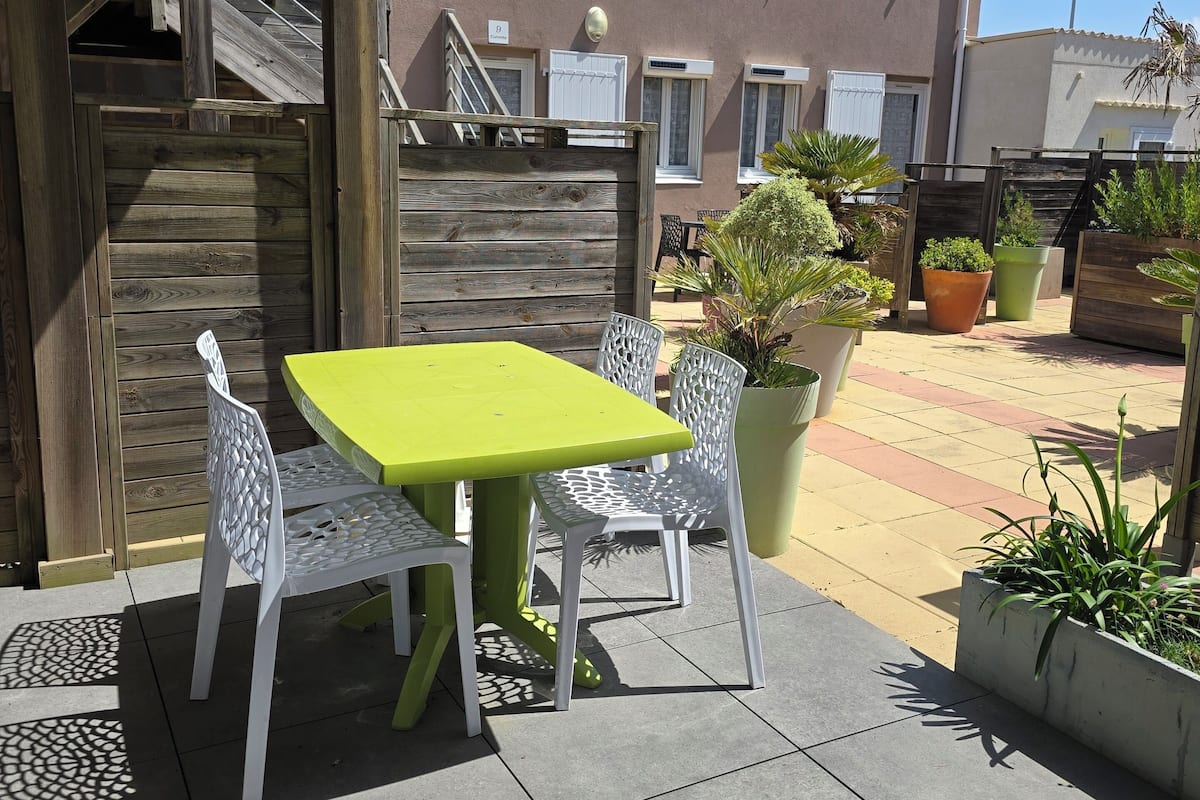 Une terrasse avec une table et des chaises, une clôture en bois et, au fond, un bâtiment doté de fenêtres en arc de cercle.