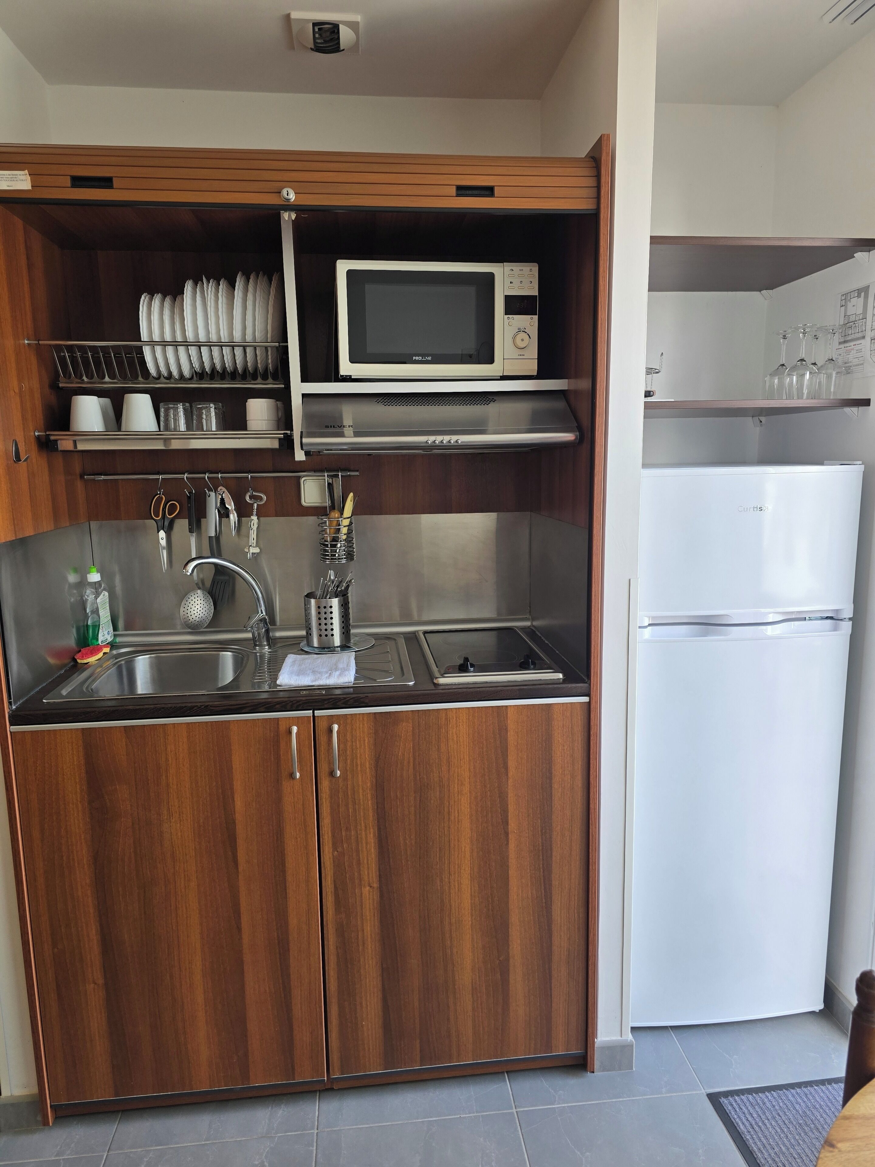 A compact kitchen with a microwave, stainless steel sink, and a refrigerator.