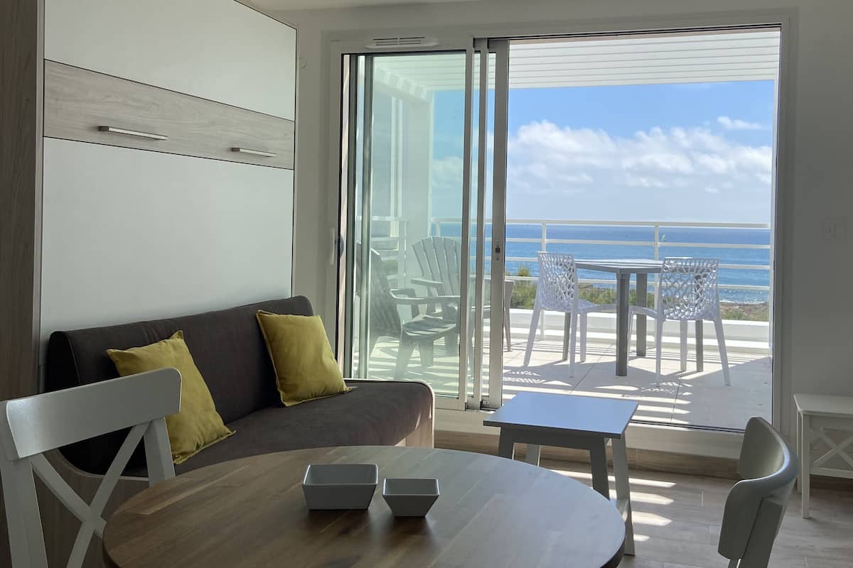 Une chambre moderne avec un canapé, une table et une vue sur l’océan, grâce à de grandes portes-fenêtres coulissantes.