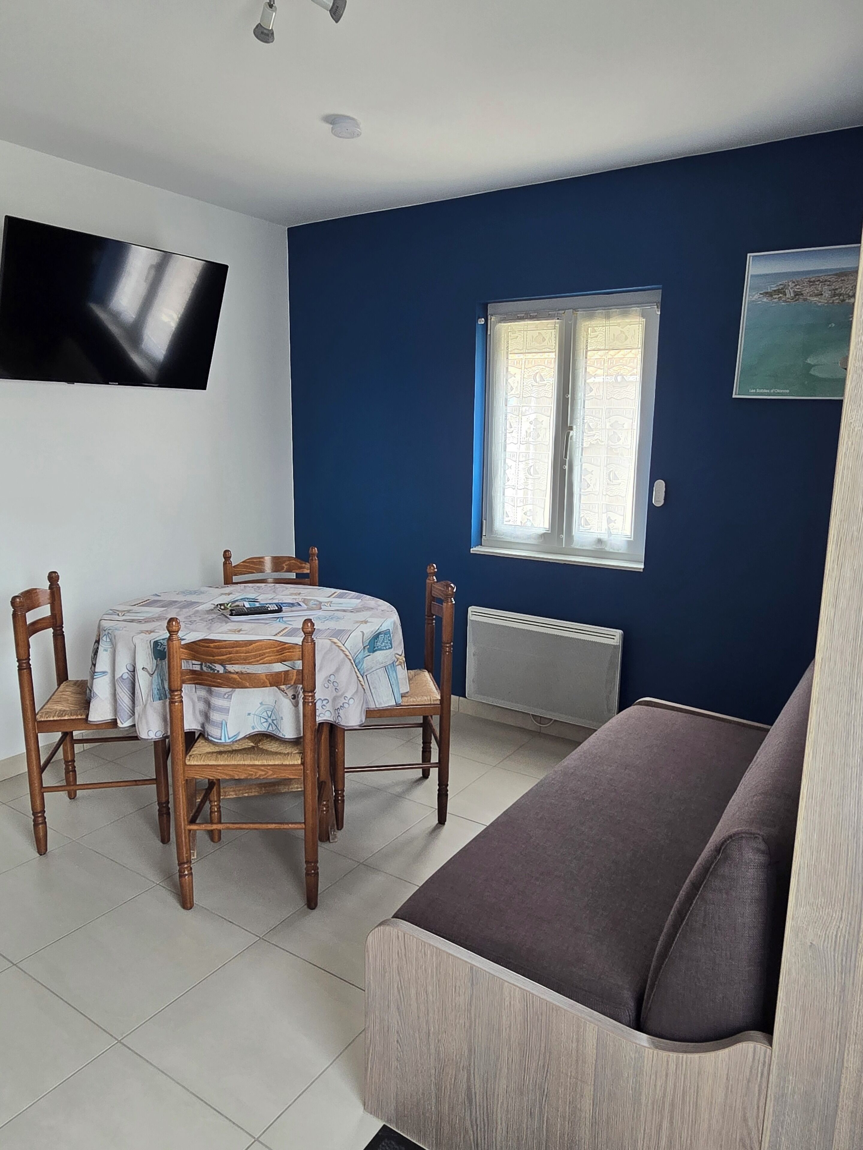 Una habitación con una mesa de comedor, sillas, un sofá, un televisor, una ventana con vistas y un radiador.