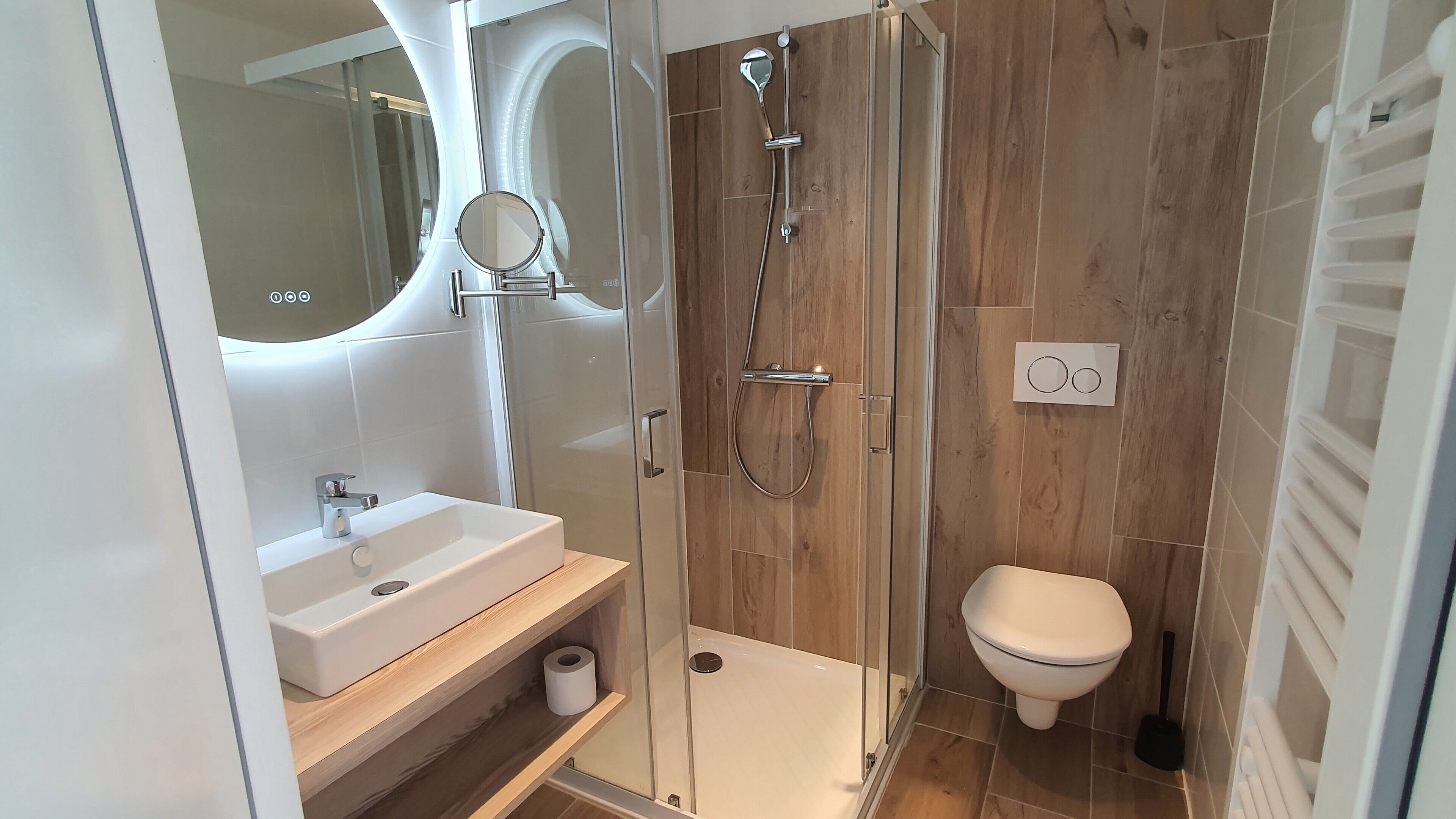 Un baño moderno con ducha de vidrio, un lavabo blanco, inodoro y espejo.