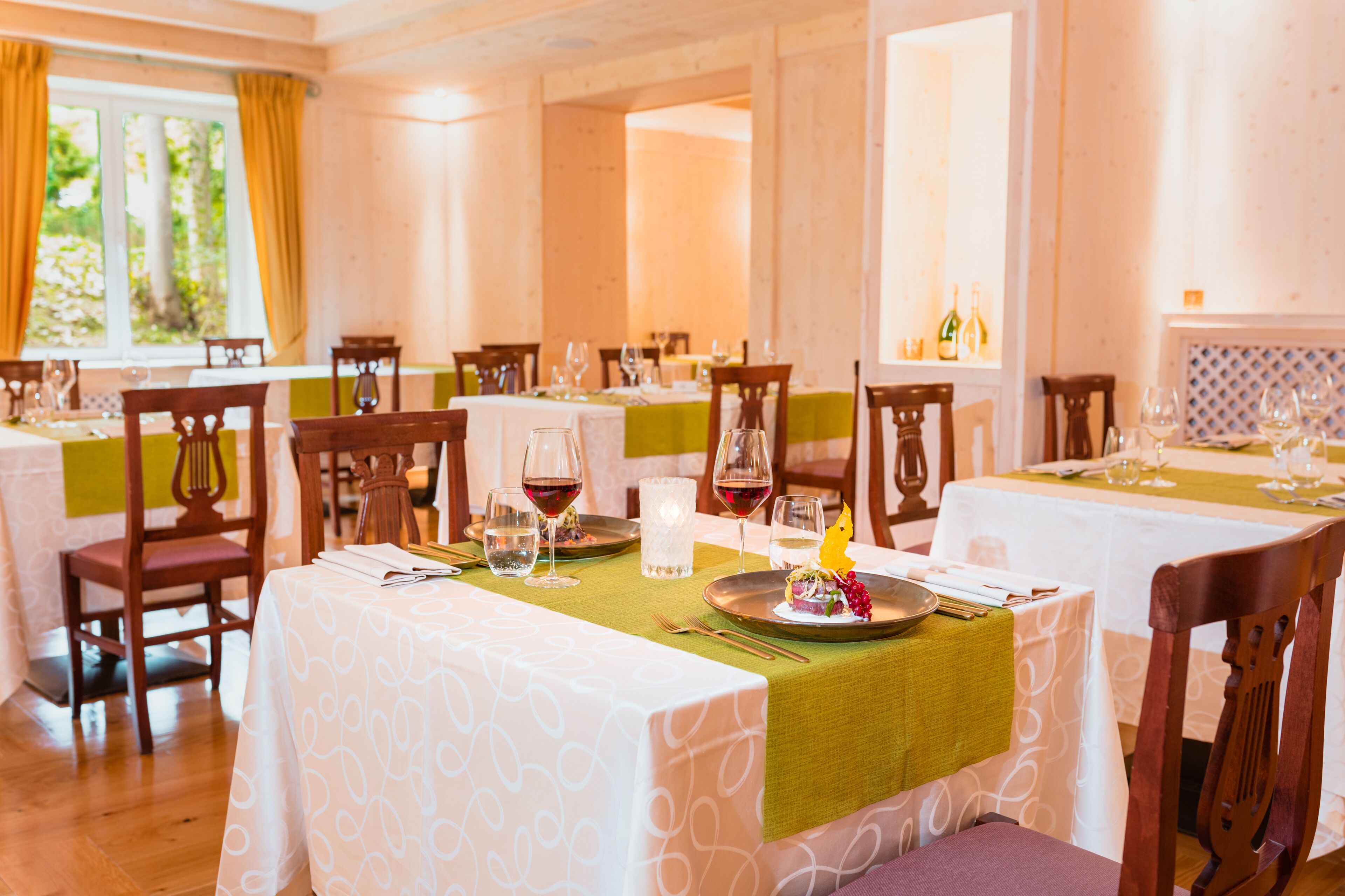 Un espace repas avec des tables dressées pour le repas, des chaises et une fenêtre avec des rideaux.