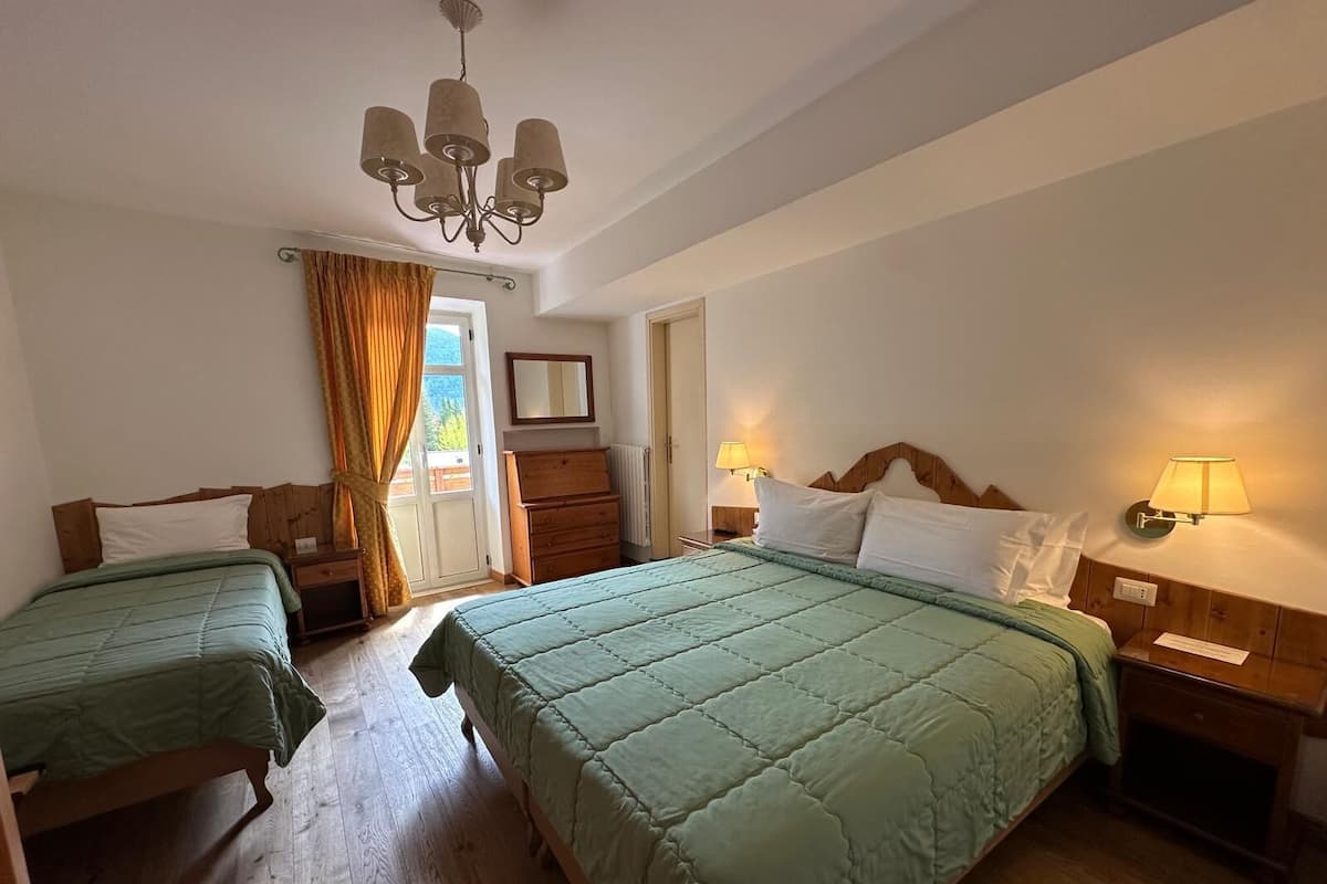 A hotel room with two beds, wooden floors, a chandelier, a dresser, and a window with curtains.