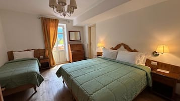 A hotel room with two beds, wooden floors, a chandelier, a dresser, and a window with curtains.