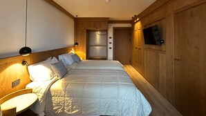 Un dormitorio con una cama grande, cabecera de madera, lámparas de noche y un televisor montado en la pared.