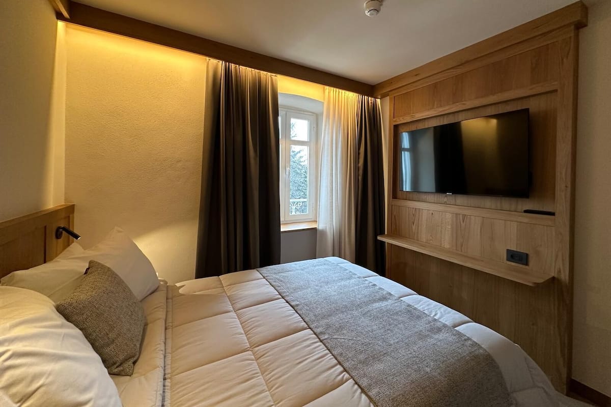 A hotel room with a bed, curtains, a TV mounted on the wall, and a window.