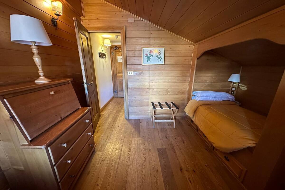 A wooden cabin room with a bed, a dresser, a lamp, and a picture on the wall.
