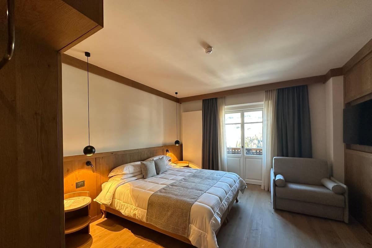 A hotel room with a large bed, a chair, a desk, and a window with curtains.