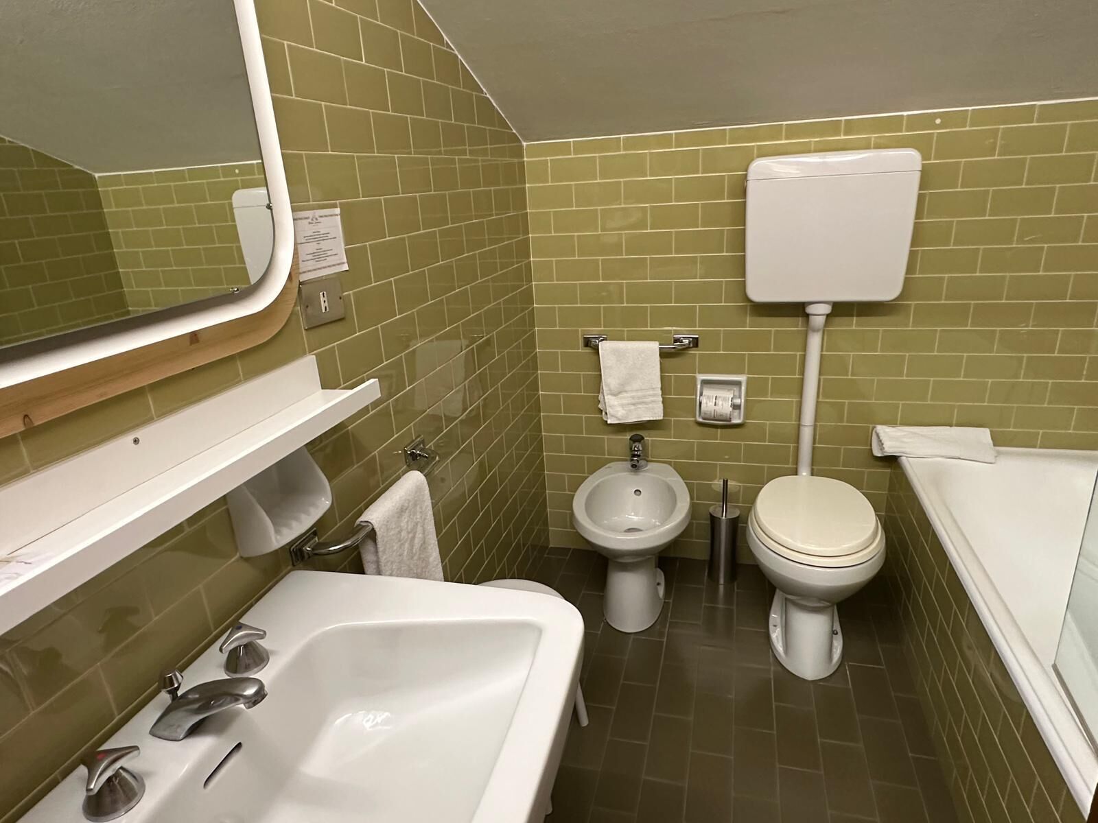 A small, clean bathroom with a sink, bidet, toilet, and a mirror.