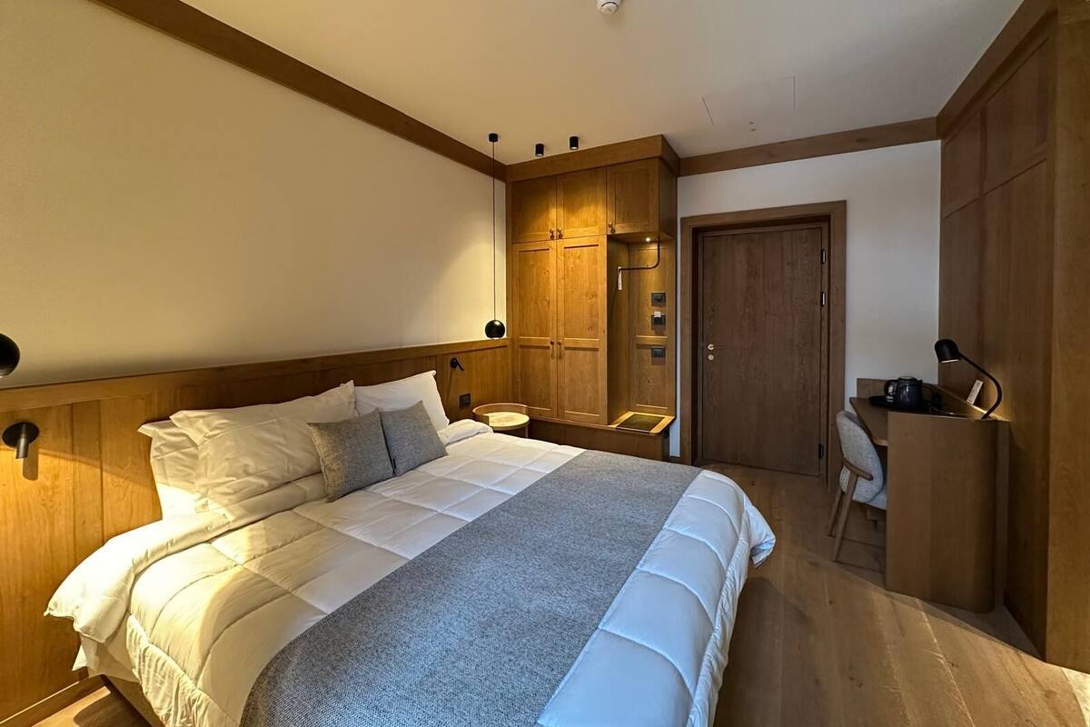 A bedroom with a large bed, wooden wardrobe, and a desk with a chair.