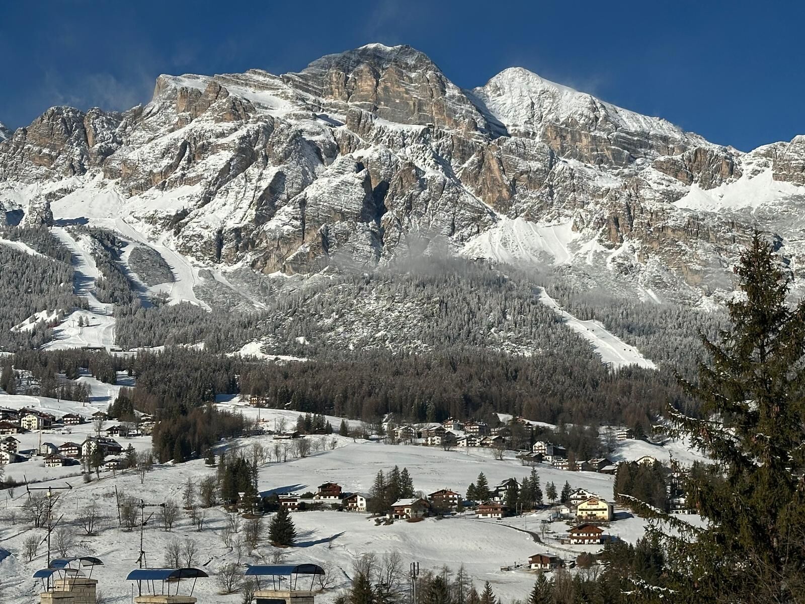 A mountainous landscape with snow-covered peaks and a village with houses and ski lifts.