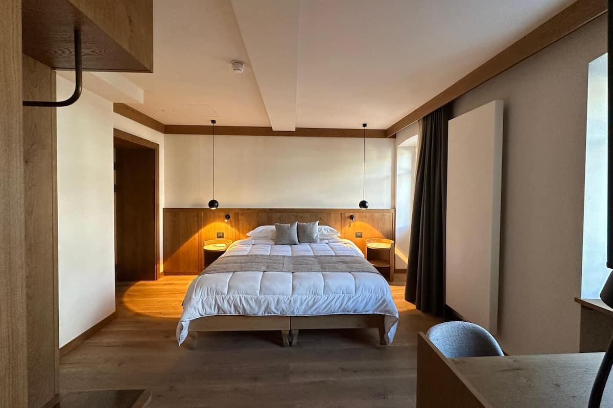 A modern hotel room with a large bed, wooden flooring, and a desk with a chair.