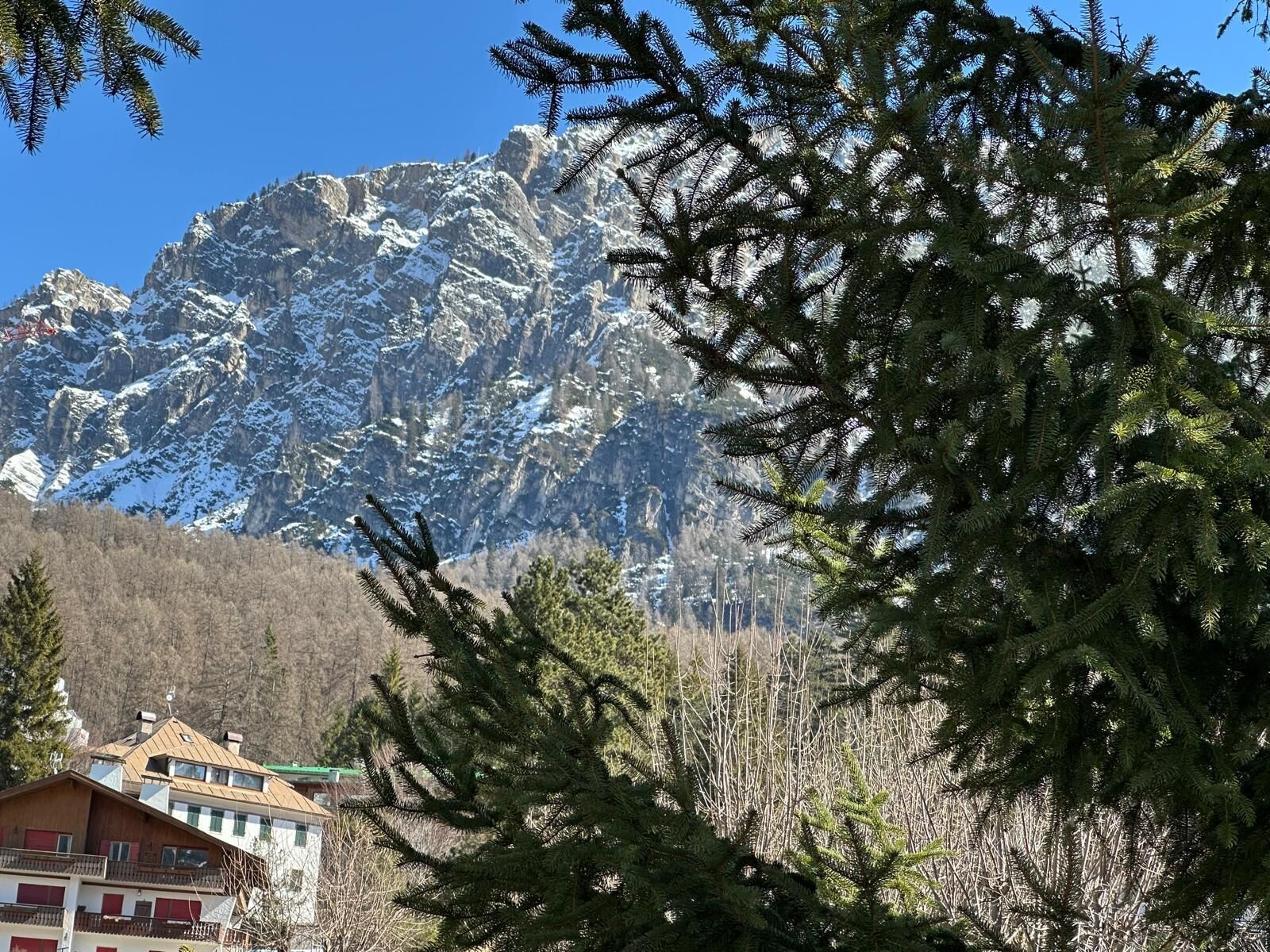 A mountain landscape with snow-covered peaks and a building with a sloped roof and red windows.