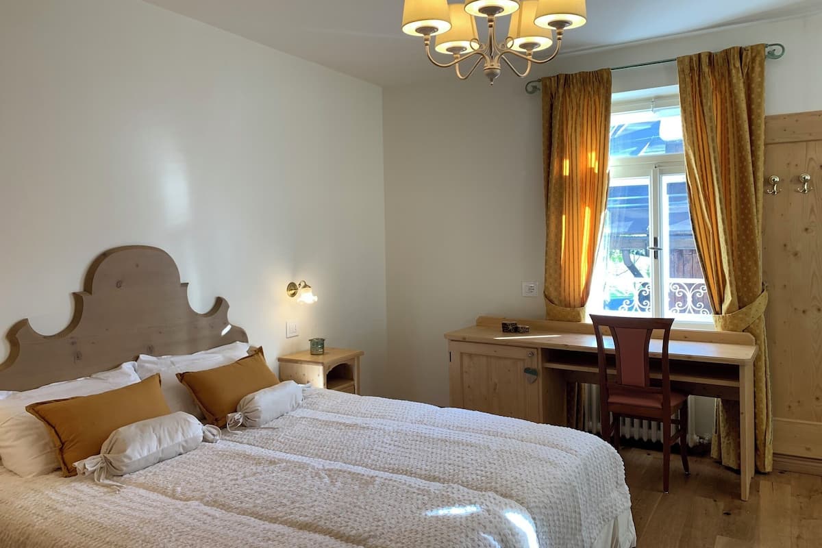 A bedroom with a bed, bedside table, lamp, and a desk with a chair.