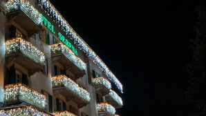 Un hotel con varios balcones decorados con luces de adorno, una entrada visible con escalones y un letrero que dice "HOTEL SERPINA".