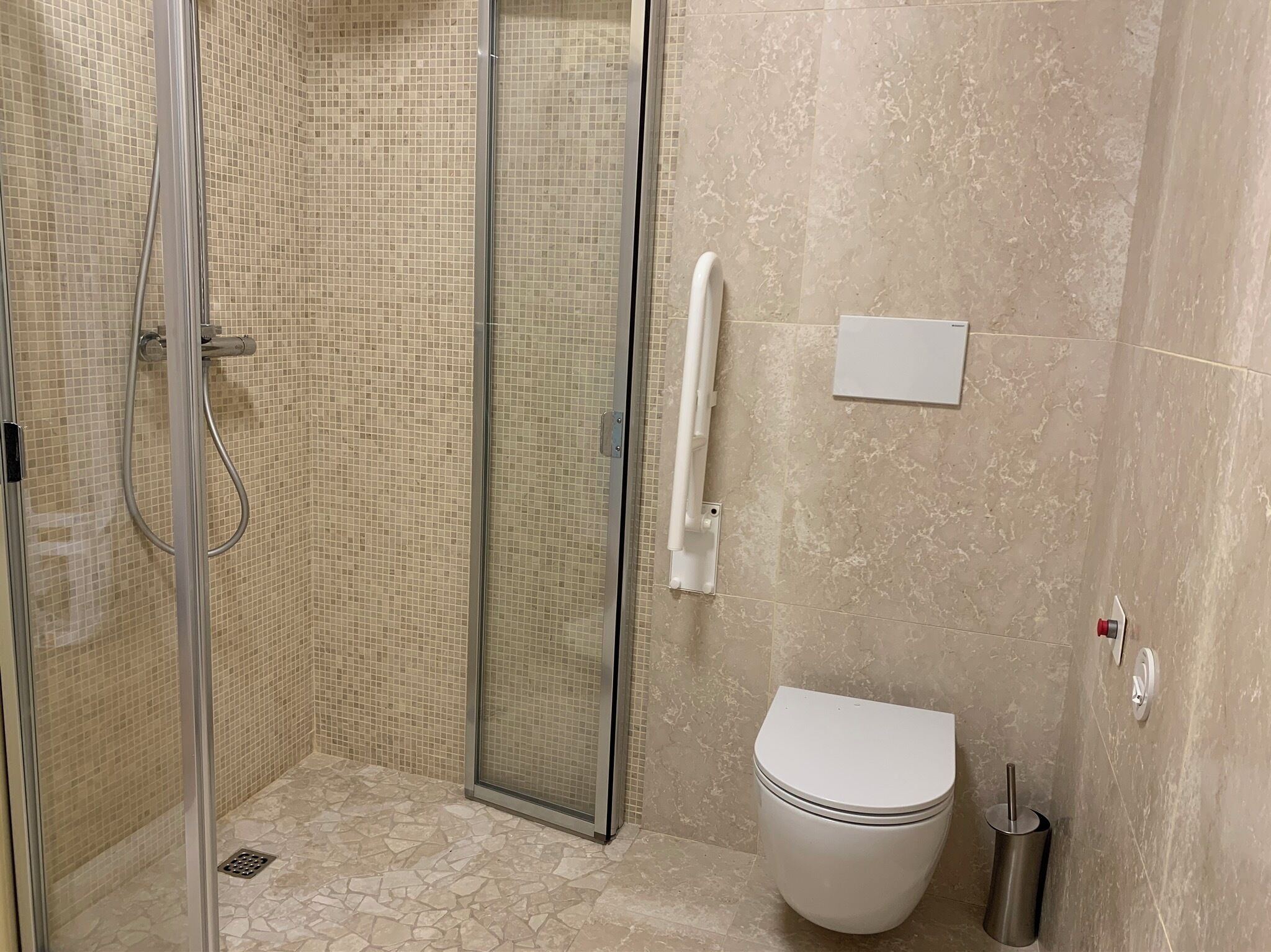 Une salle de bain avec une douche à parois de verre, des toilettes blanches et une barre d’appui.