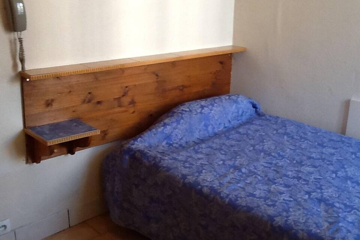 Un dormitorio con cabecera de madera, una pequeña estantería y una colcha azul.