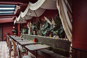 Un restaurante con una barra larga, asientos acolchados y plantas tropicales.