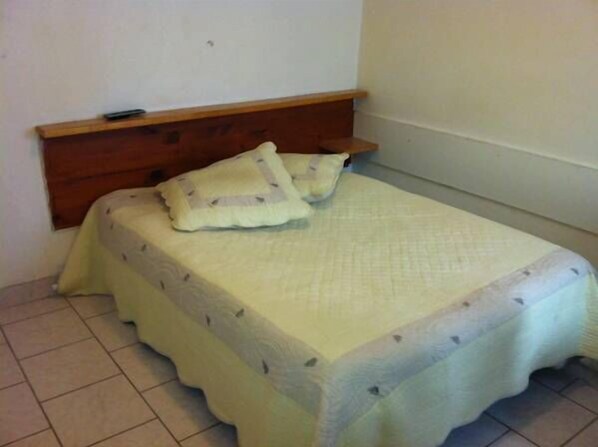 Ein kleiner, schlichter Raum mit einem Bett, einem Holzkopfende und einer schlichten Wand.