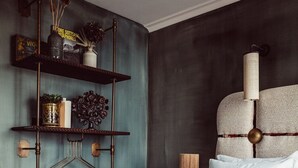 Un dormitorio con cama, manta azul con textura, lámpara colgante y repisa con adornos.