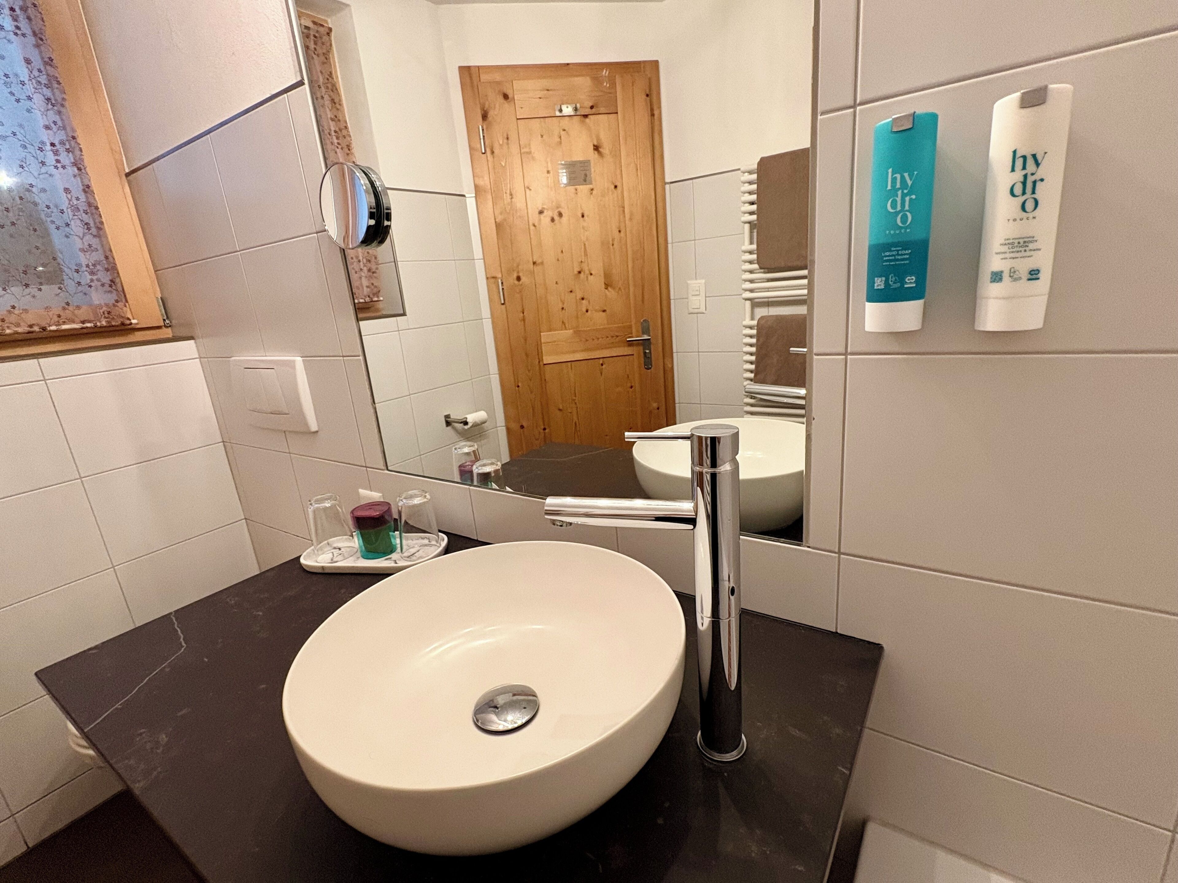 Un baño con un lavamanos blanco, un espejo y una puerta de madera. Hay artículos de tocador en el mostrador.