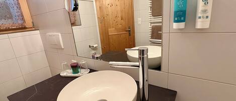 Un baño con un lavamanos blanco, un espejo y una puerta de madera. Hay artículos de tocador en el mostrador.