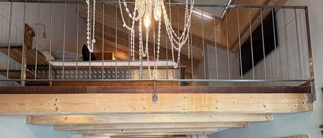 A loft-style living space with a wooden ceiling, a staircase, a sofa, a coffee table, and a TV mounted on the wall.