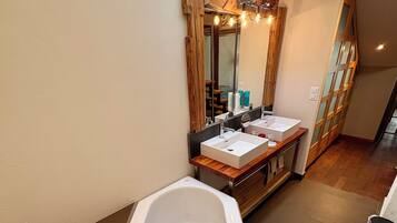 A modern bathroom with a large bathtub, two sinks, and a wooden-framed mirror with lights.