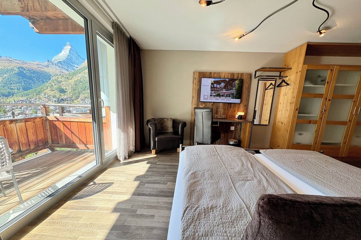 Une chambre d’hôtel avec une grande fenêtre, un lit, un bureau, une chaise et une armoire.