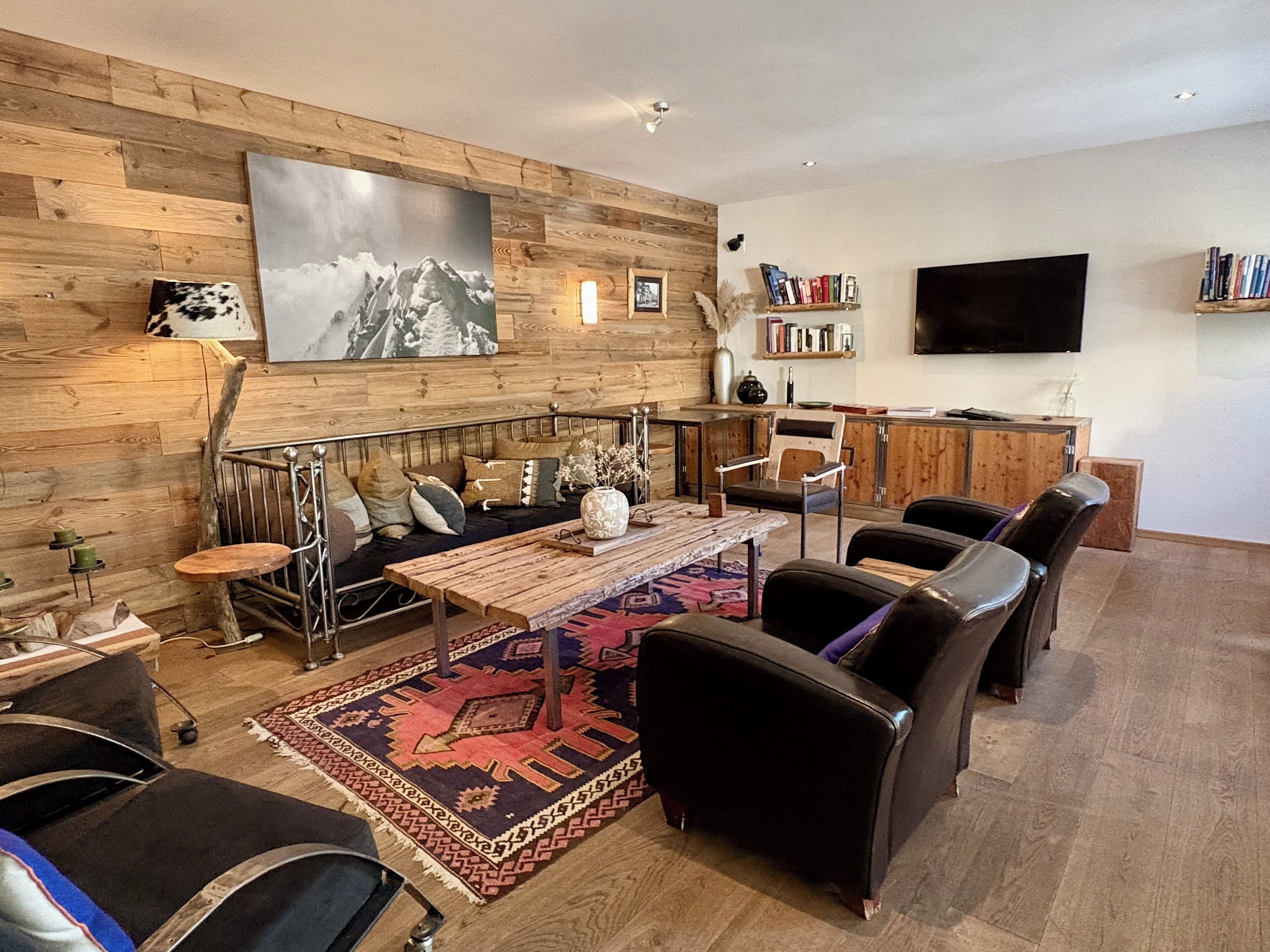 Ein modernes Wohnzimmer mit einer Holzwand, einem großen Gemälde, einer Couch mit Kissen, einem Couchtisch, einem Teppich und einem Fernseher.