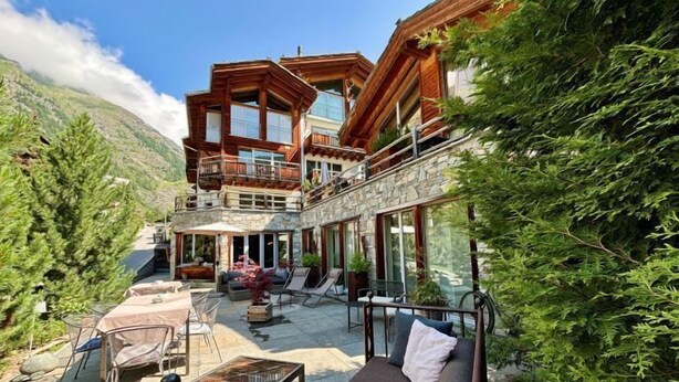 A two-story building with a stone facade, a balcony, and outdoor seating area with tables and chairs. - Alpenlodge (Zermatt)