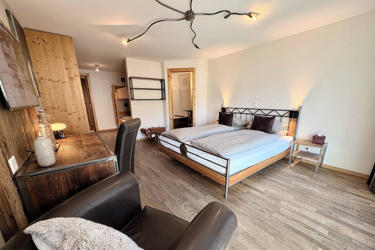 Une chambre moderne avec un grand lit, un bureau en bois, une chaise et un miroir.