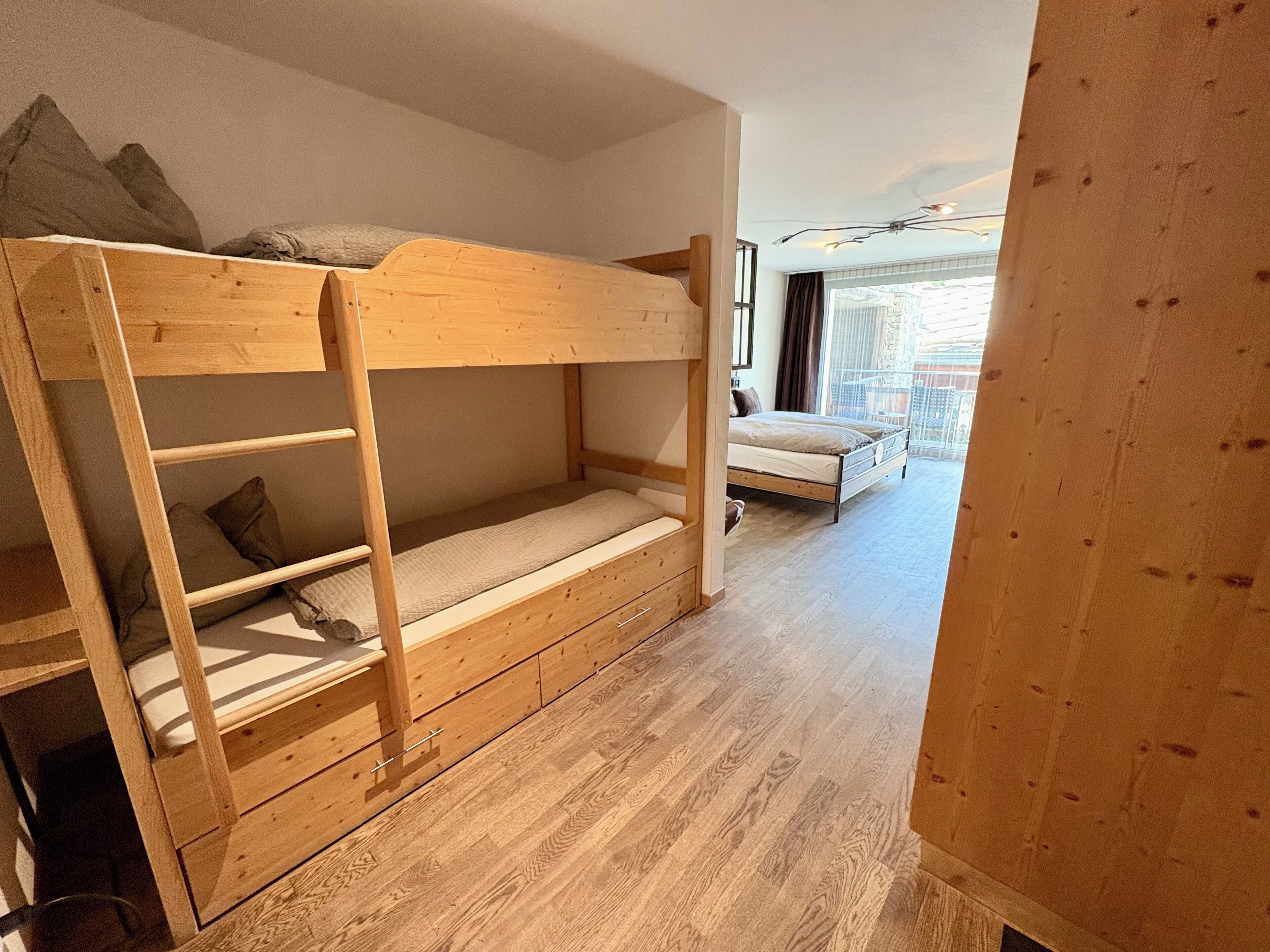 Un lit superposé avec une échelle, un lit simple et un plancher en bois.
