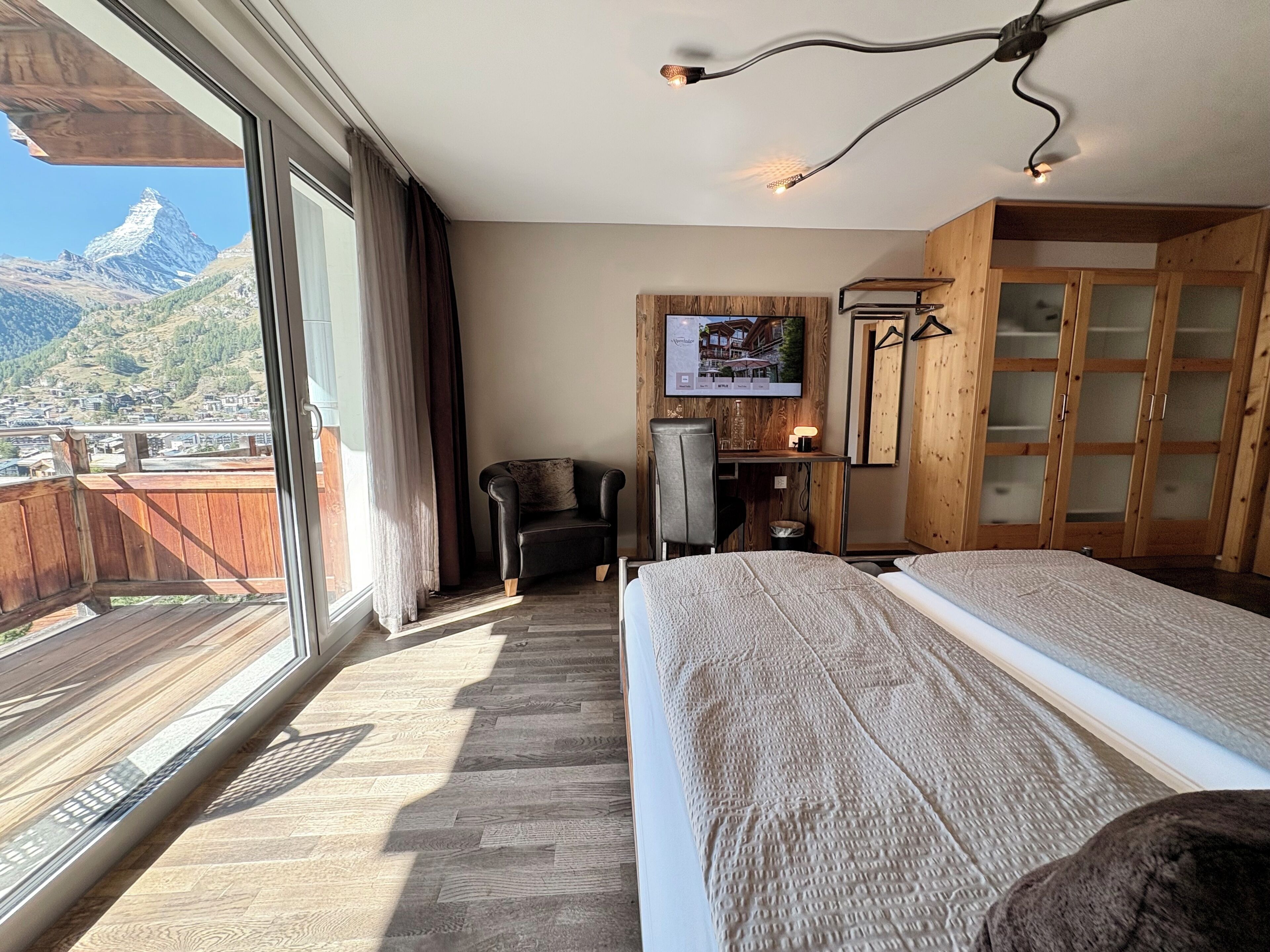 Habitación de hotel con cama, escritorio, silla, televisor y vistas a las montañas.