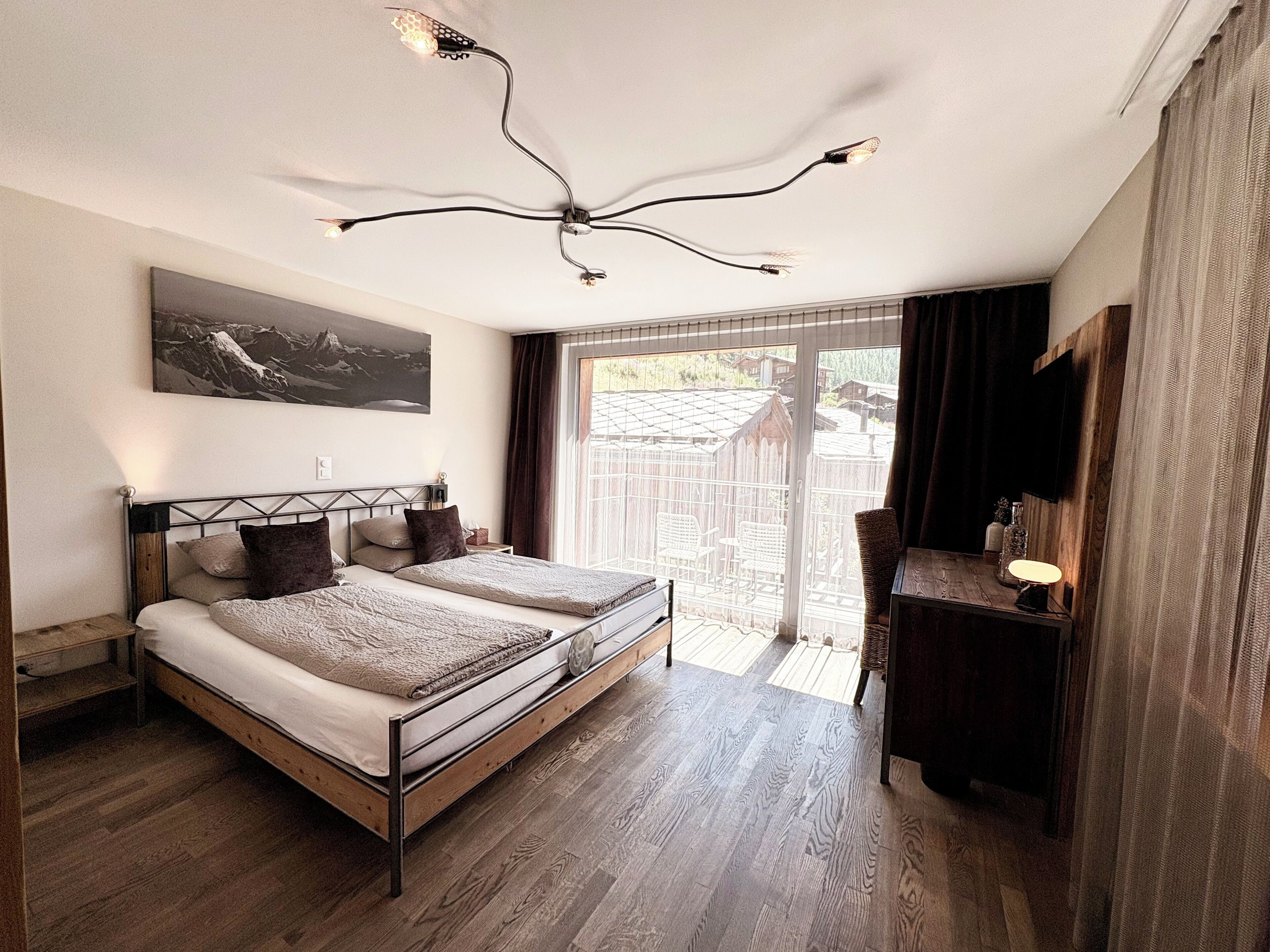 Une chambre à coucher avec un lit en bois, un bureau avec une lampe et une grande fenêtre donnant sur l’extérieur.