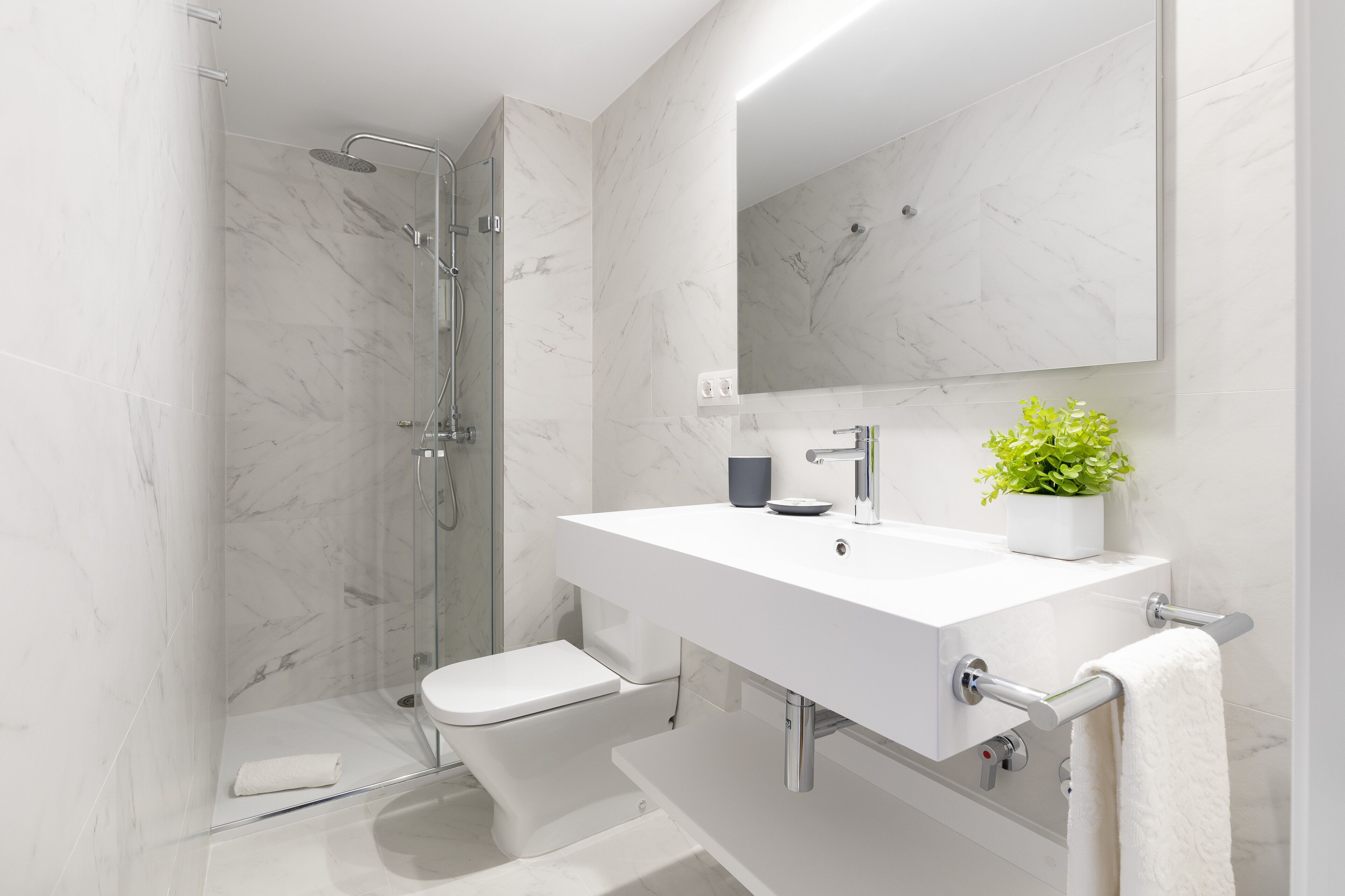 Ein modernes Badezimmer mit einer begehbaren Glasdusche, einem weißen Waschbecken und einem Spiegel darüber.