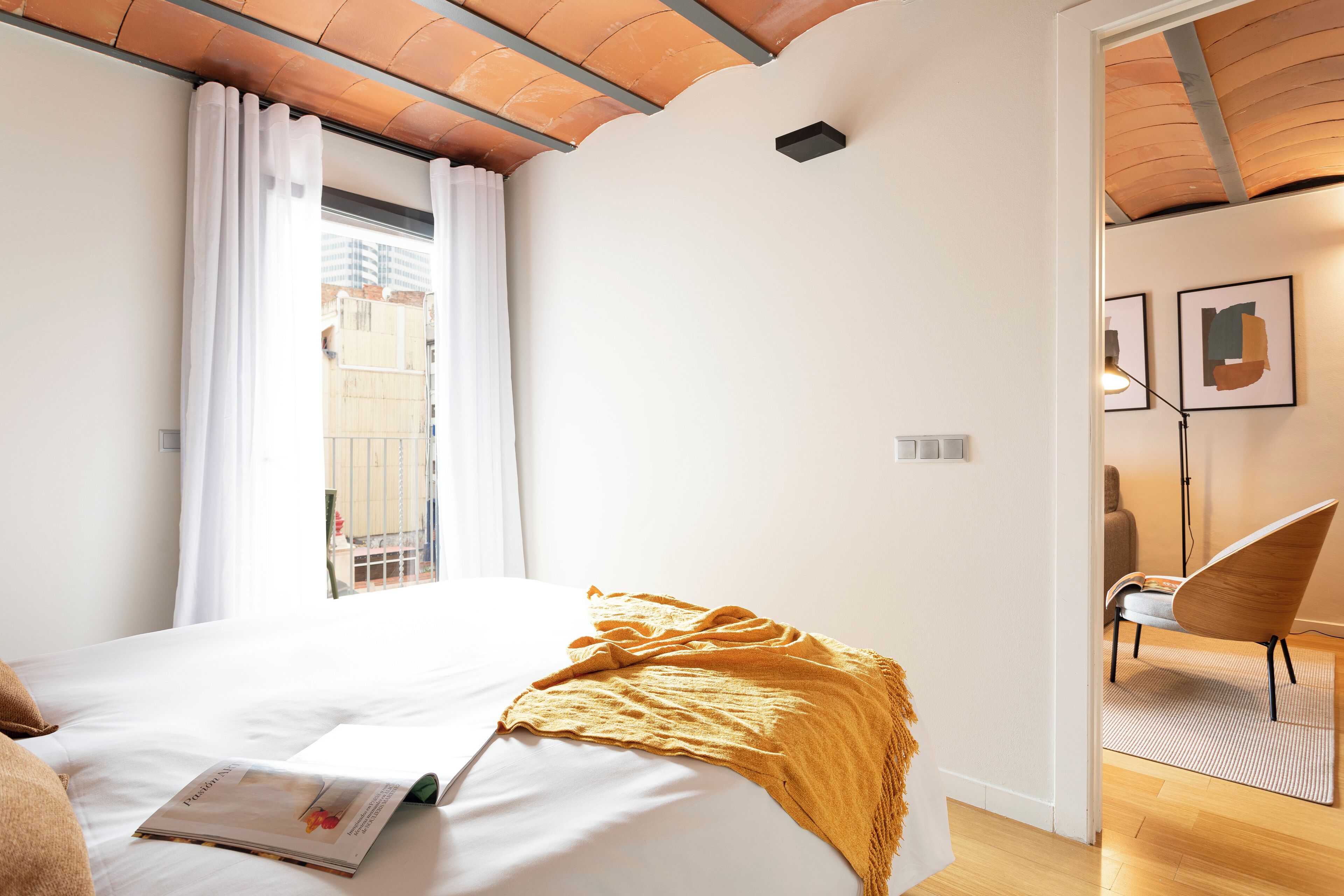 Ein Hotelzimmer mit Bett, einem Vorhangfenster, einem Sessel und einem Kunstwerk an der Wand.