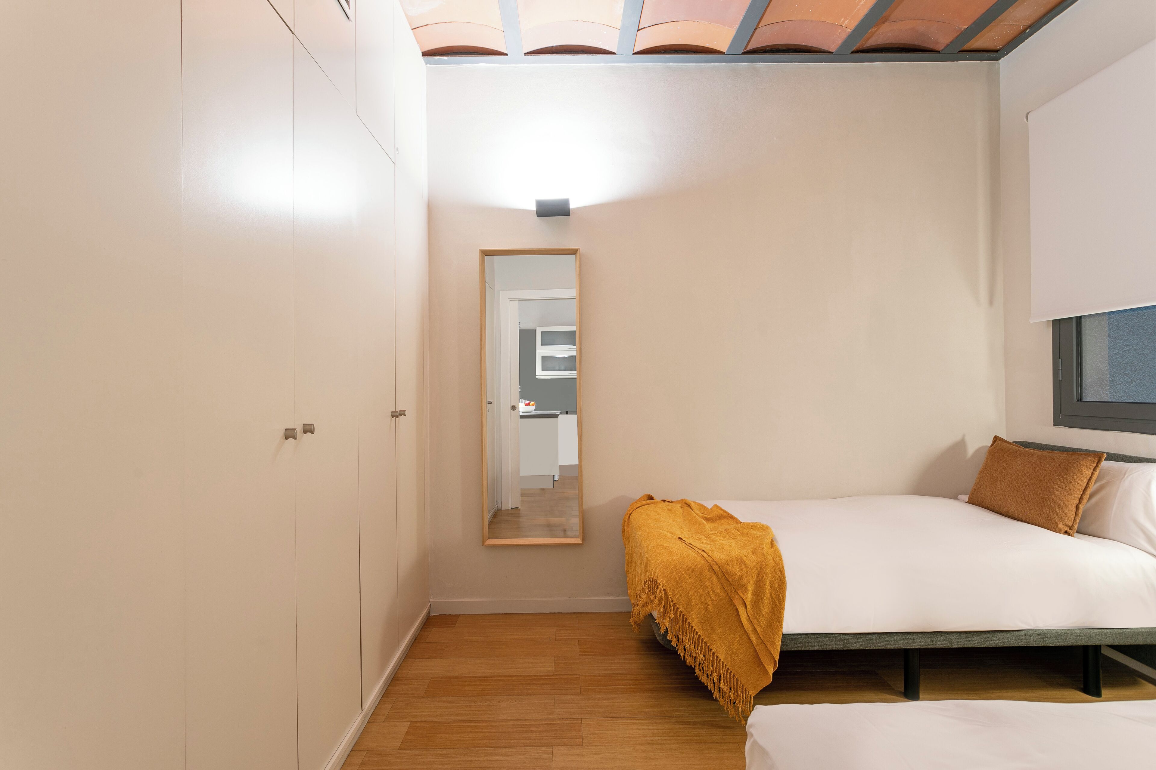 A bedroom with a bed, a bedside table, a mirror, and a wardrobe.
