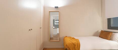A bedroom with a bed, a bedside table, a mirror, and a wardrobe.
