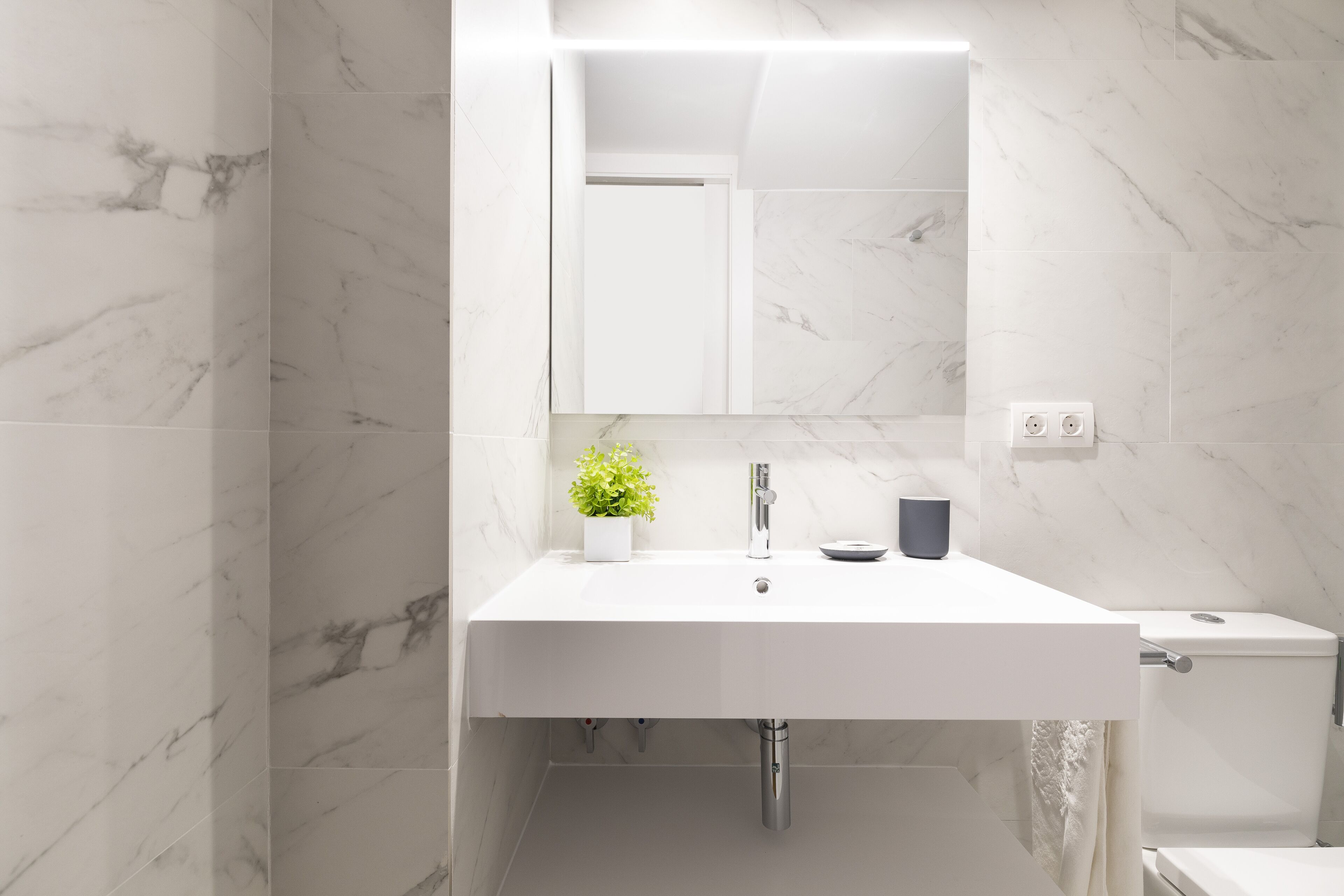 Une salle de bain moderne avec un lavabo blanc, un miroir au-dessus et des toilettes sur la droite.