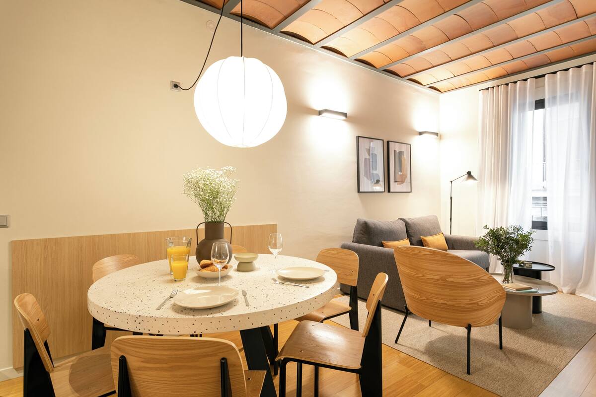 A modern dining area with a round table, chairs, and a hanging light fixture.