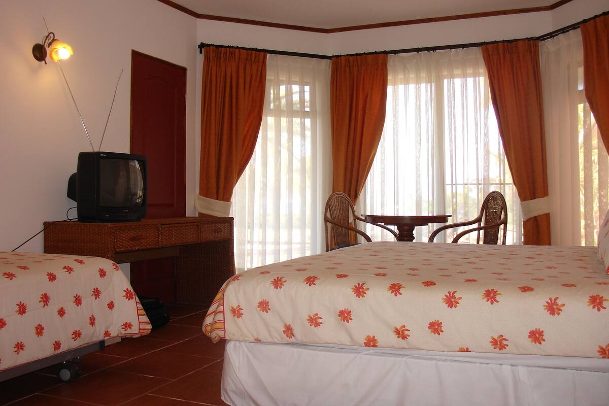 A hotel room with two beds, a desk with a television, a chair, and a table.
