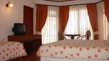 Een hotelkamer met twee bedden, een bureau met een televisie, een stoel en een tafel.